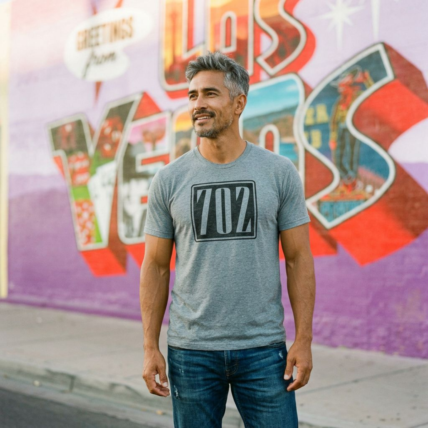 702 Square Las Vegas area code t-shirt in premium heather, full-length shot in front of the Greetings from Las Vegas mural