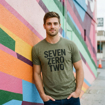 Man leaning against a colorful mural in the military green Seven Zero Two Las Vegas T-shirt