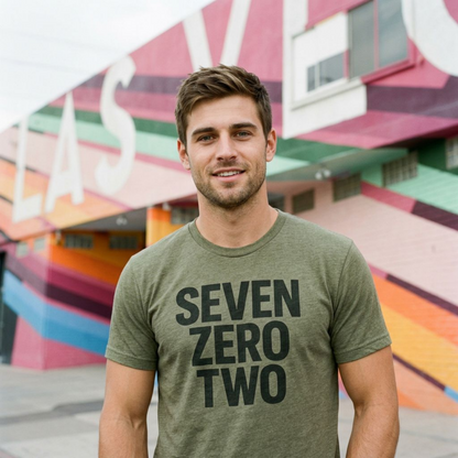Close-up of a man wearing the military green Seven Zero Two Las Vegas T-shirt by a colorful mural